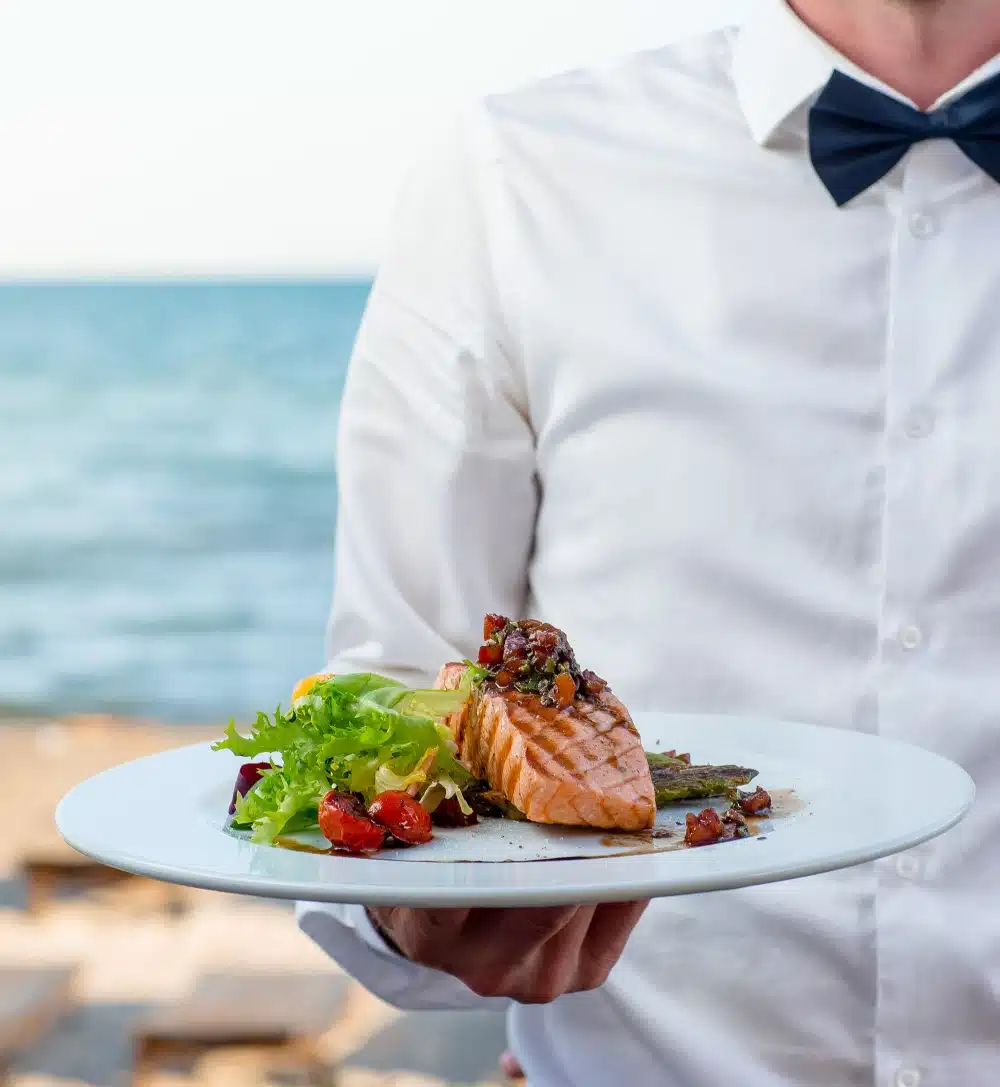 waiter holds plate grilled smoked salmon with lettuce tomato pepper
